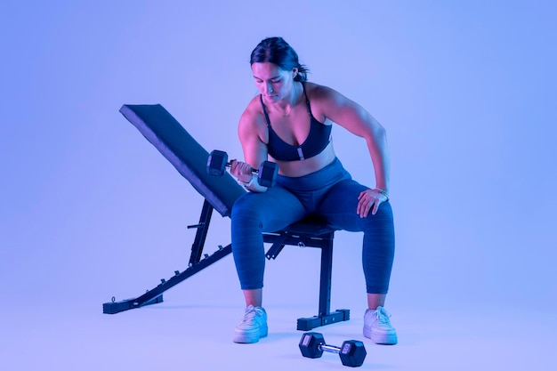 Woman in sportswear doing biceps exercises sitting on a bench