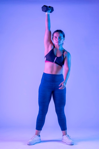 Woman in sportswear doing dumbbell snatch on a colored background