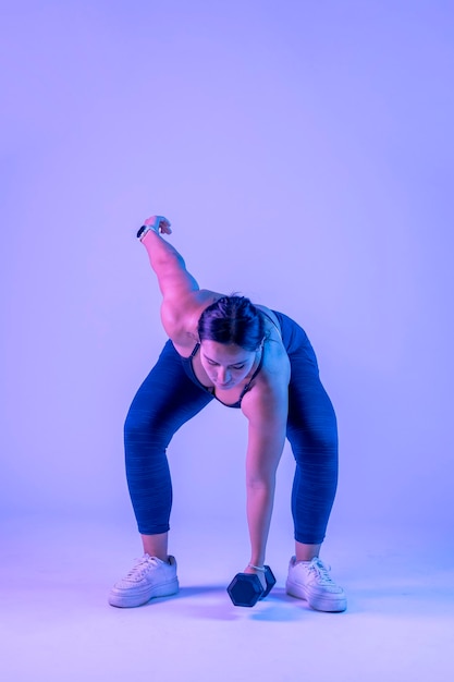 Woman in sportswear doing dumbbell snatch on a colored background