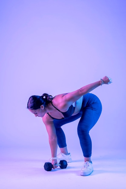 Woman in sportswear doing dumbbell snatch on a colored background