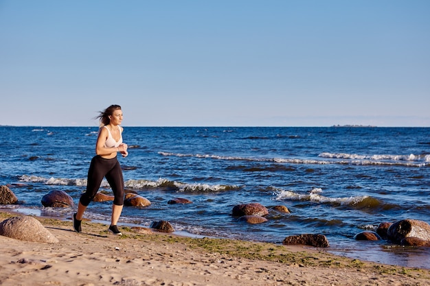 Woman in sportswear is running near shore