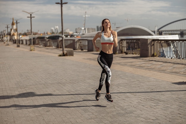 Woman in sportswear and sneakers runs along empty city waterfront