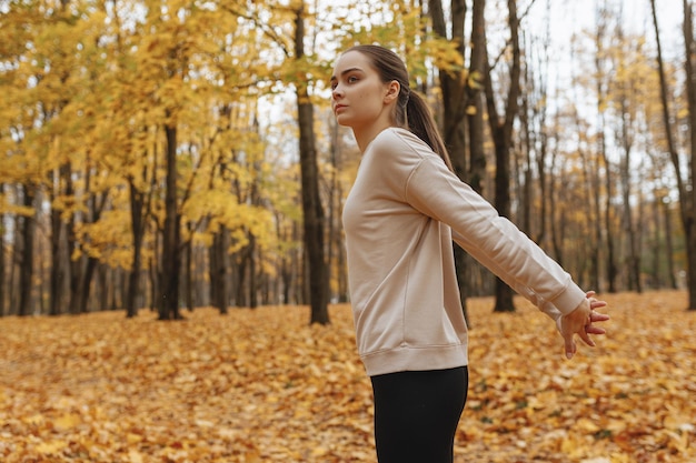 woman in sportswear stretching arms behind back while training in park