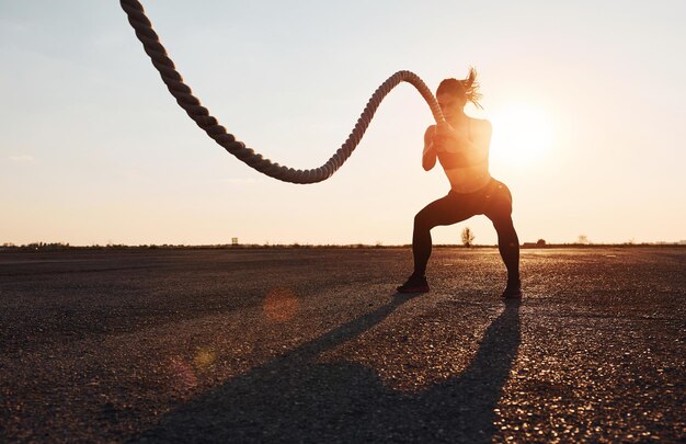 Woman in sportswear training with knots on the road at evening time