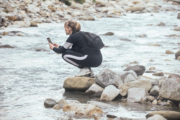 A woman in sportswear and with a backpack takes pictures of nature in the mountains on the phone