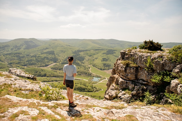 Woman in sporty uniform and sneakers is standing on mountains peak