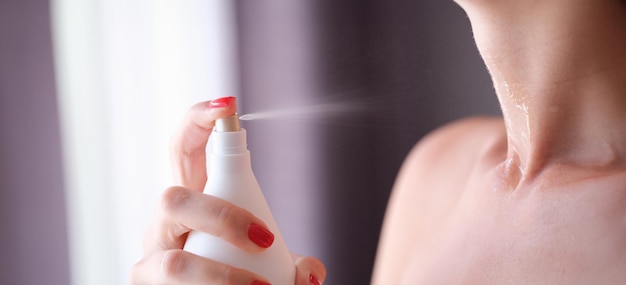 Woman spraying perfume or moisturizing skin lotion on neck closeup