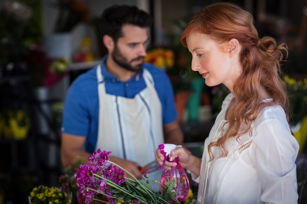 Photo woman spraying water on bunch of flowers while man preparing flower bouquet