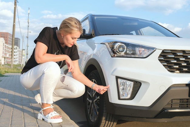 Woman squats down in front of her car and looks at a scratch on the bumper