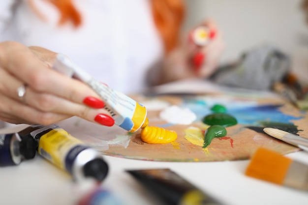 A woman squeezes yellow paint from a tube onto a palette for painting female hands with