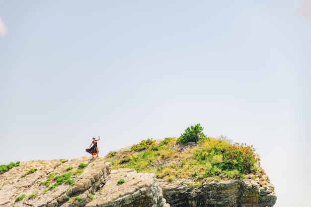 Woman stand on the cliff in light dress at sunny day