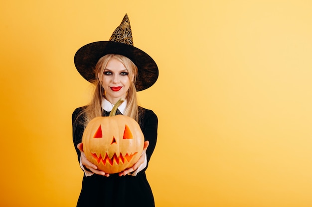 Woman standing against a yellow   holding pumpkin and showing it on straight hands