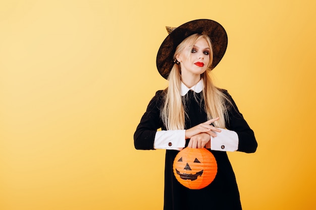 Woman standing against a yellow   holding pumpkin.