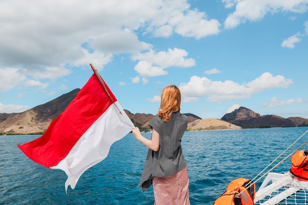 A woman standing on a boat and waving indonesia flag in the middle of sea