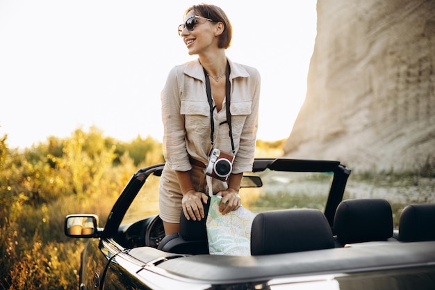 Woman standing in cabriolet on the mountain sunset holding map and camera