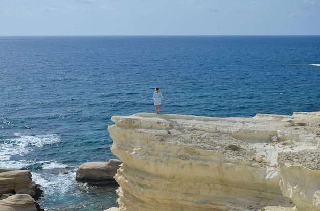 Woman standing on a cliff near sea and look at the waves