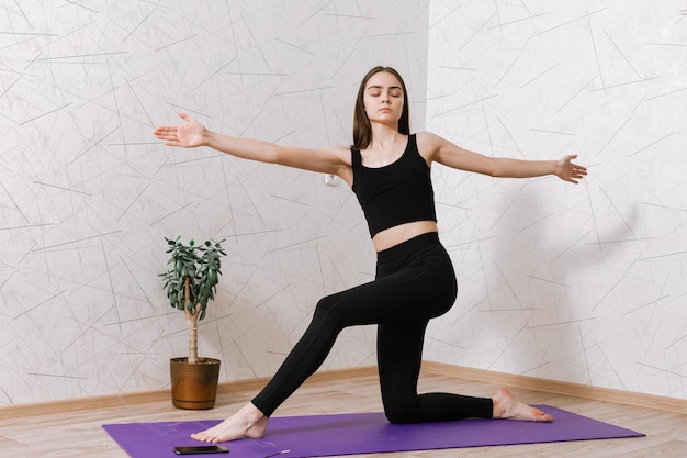 woman standing in Crescent Lunge asana on mat with closed eyes and practicing yoga on mat