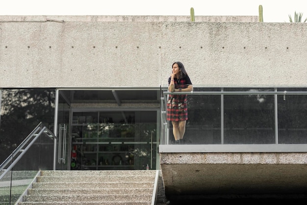 Woman standing on the facade of a building leaning on the railing looking at the horizon copy space