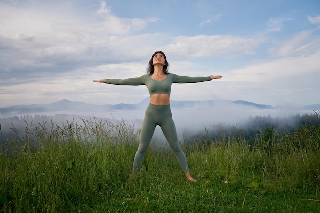 Woman standing on grass on mountain hill in pose of winner