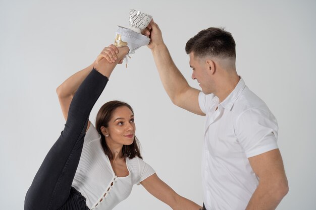 Woman standing in gymnastics split and man near holding cup with beverage on her fit isolated on whi...