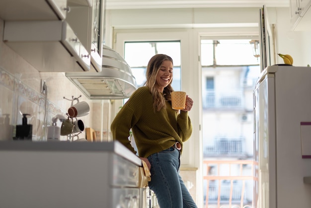 Woman standing in the kitchen and drinking cup of tea