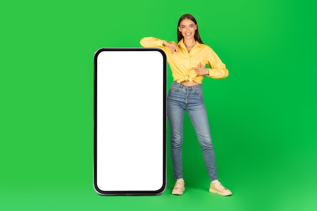 Woman standing near huge phone pointing at screen green background