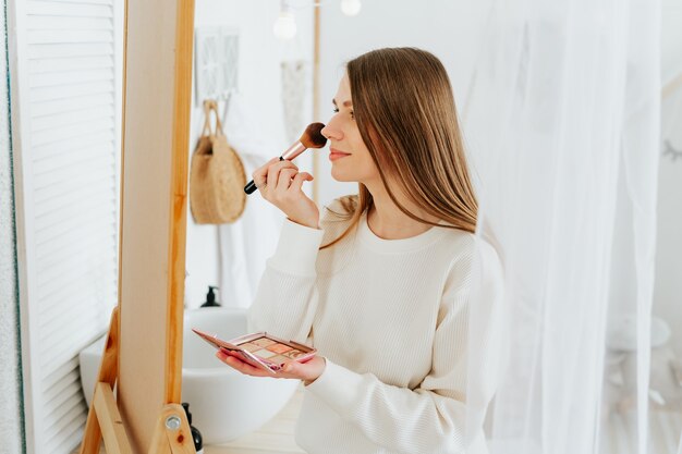 Woman standing near mirror and doing makeup