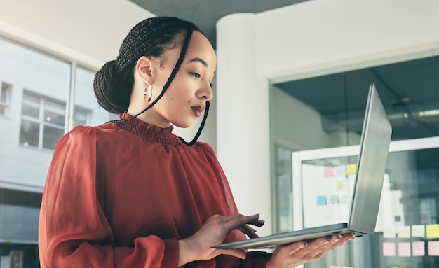 Woman standing in office with laptop research and ideas on website for business plan brainstorming or proposal process Thinking typing and businesswoman on computer with online review at startup