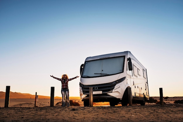 Woman standing outstretching arms and enjoying freedom and travel lifestyle with modern camper van