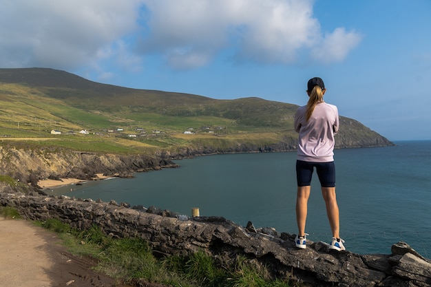 Woman standing on stone wall looking at cliffs on Dingle peninsula Ireland