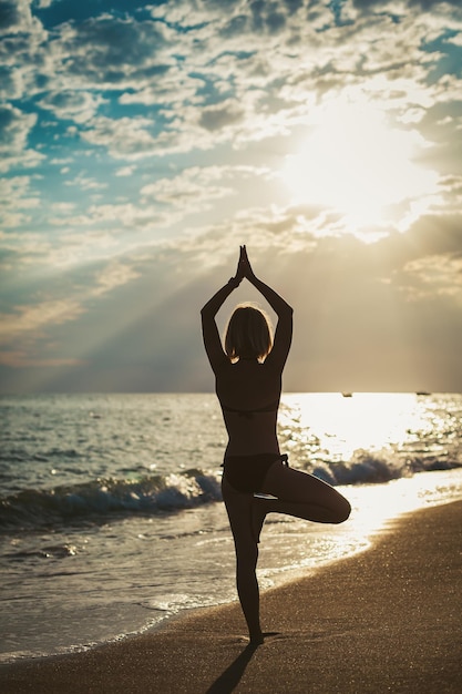 Woman standing in a Tree position on the beach