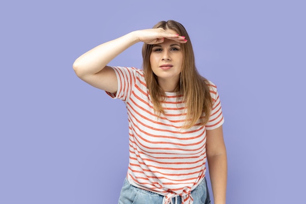 Woman standing with hand near forehead and looking far away looks at distance