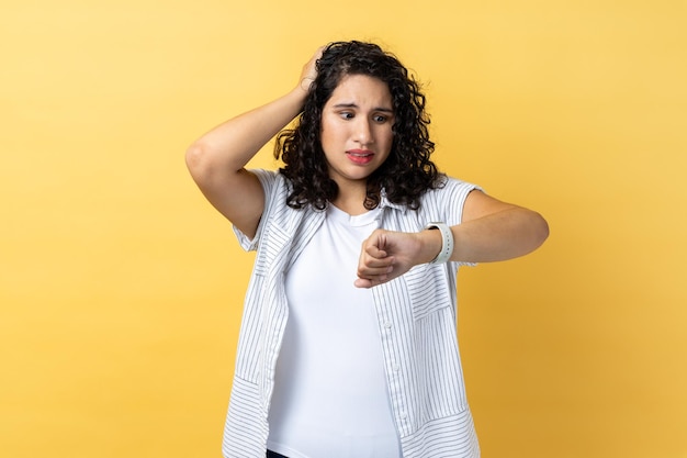 Woman standing with puzzled facial expression worried about deadline looking at wristwatch