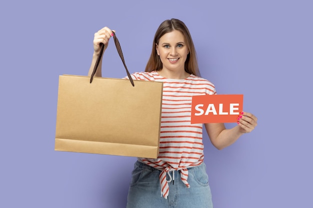 Woman standing with sale card and shopping bag in hands presenting discounts