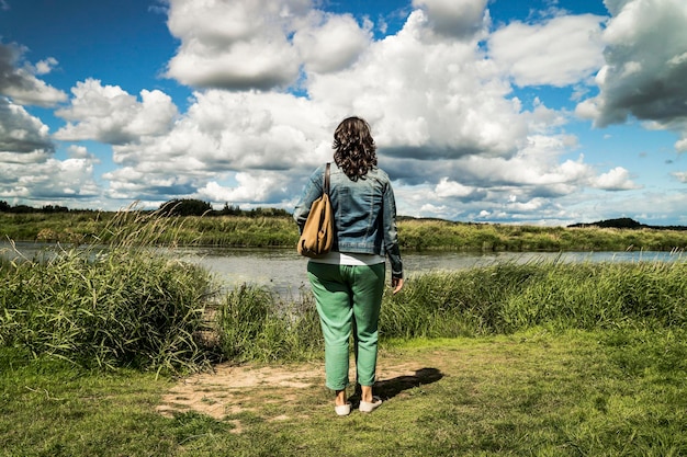 Woman stands on the bank of a small river and looks into the distance