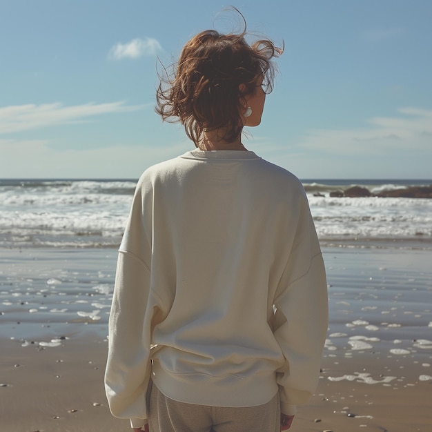 a woman stands on a beach with the ocean in the background Sweatshirt mockup back view