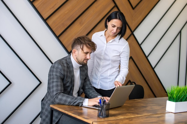 A woman stands next to a man sitting at a desk with a laptop in the office