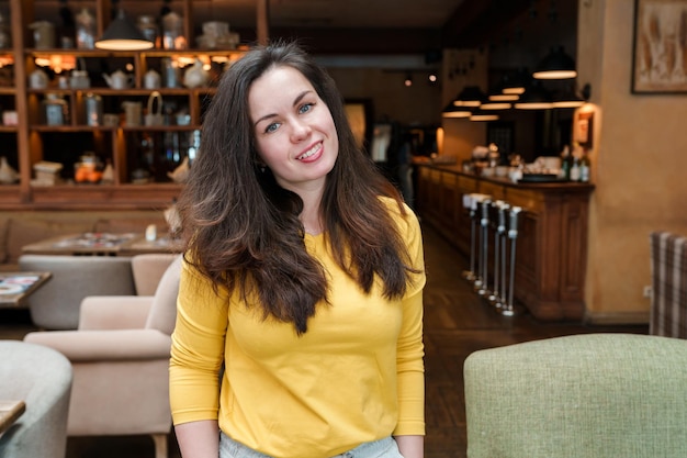 A woman stands in a restaurant with a bar in the background.