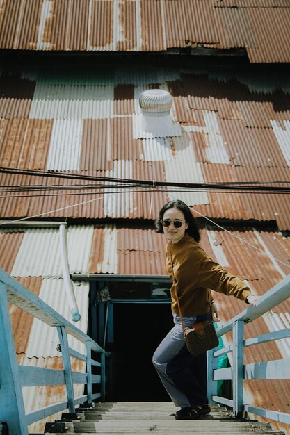 A woman stands on a staircase in front of a corrugated iron roof.