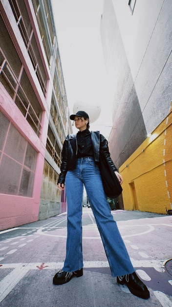 A woman stands in a street in front of a pink building.