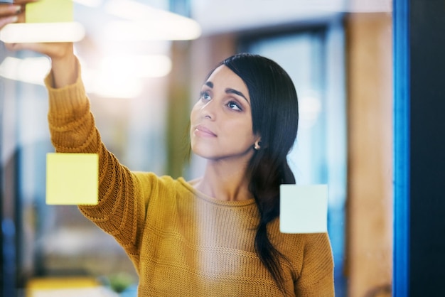 Photo woman sticky note and glass wall in office for ideas planning or brainstorming at company person thinking and paper on board for problem solving solution or process for job at creative agency