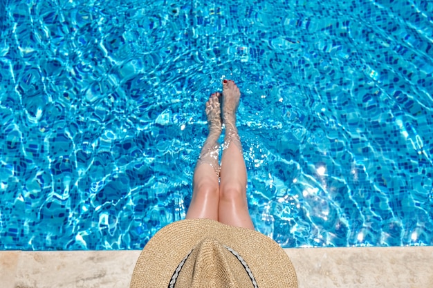 Woman in straw hat sitting in the swimming pool with legs in water