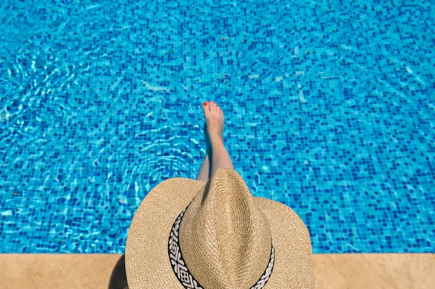 woman in straw hat sunbathing sitting on the edge of swimming pool