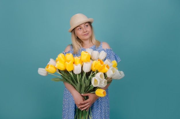 Photo woman in straw hat wearing blue dress  with white and yellow tulips in her hands. summer and spring concept.