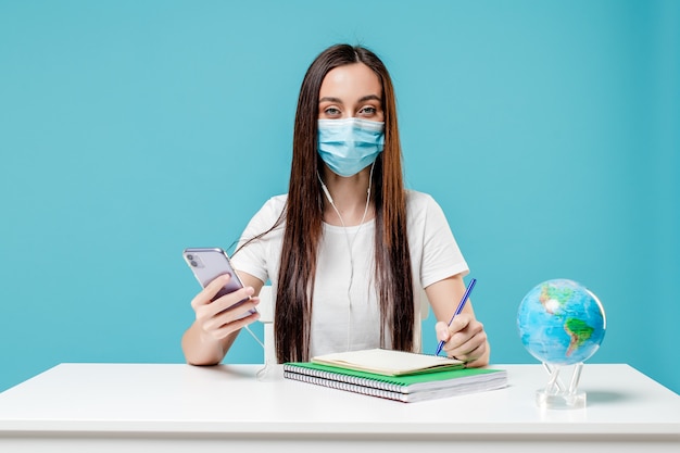 Woman studying with planet earth globe and phone with books wearing mask