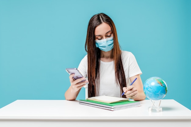 Woman studying with planet earth globe and phone with books wearing mask