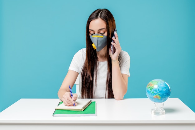 Photo woman studying with planet earth globe and phone with books wearing mask