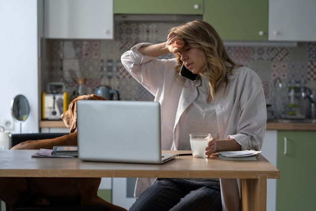 Woman suffer from migraine talking on cellphone holding glass with headache effervescent tablet