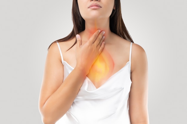 A woman suffering from acid reflux or Heartburn on gray