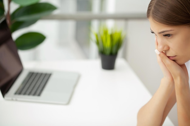 Woman suffering from toothache and touching her cheek while sitting at her desk